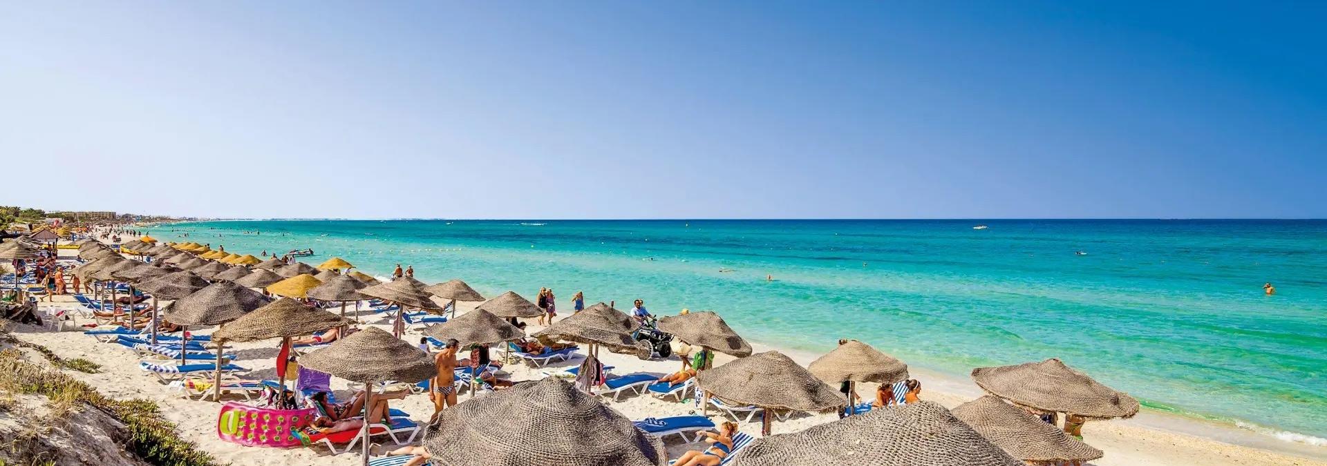 Tyrkysové more, svetlý piesok a lehátka so slnečníkmi na tuniskej pláži v Mahdii.