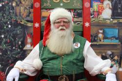 Santa Claus sediaci na kresle vo svojej kancelárii so stromčekom. 