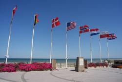 Vlajky a pamätník pri mori v Arromanches. Francúzsko