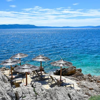 Kamenisté pláže pri meste Rabac so slnečníkmi.