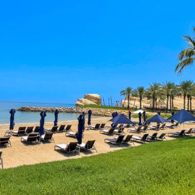 Jasná obloha, pokojné more a pobrežie s lehátkami pred hotelom v Muscate.