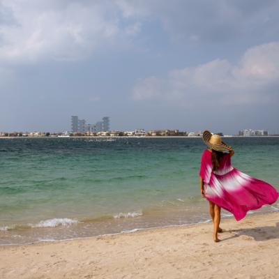 Žena v ružových šatách kráča po pieskovej pláži v Dubaji.