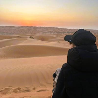 chlapec pozoruje východ slnka na púštnej dune Wahiba, MUscat, Omán