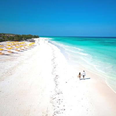 Exotický Zanzibar s bielymi plážami, lehátkami a prechádzajúci sa pár.