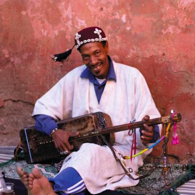Marocký hudobník Gnawa sediaci na zemi s gitarou.