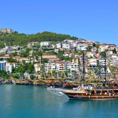 Mesto Alanya s prístavom a loďou, promenádou a hradom na kopci.
