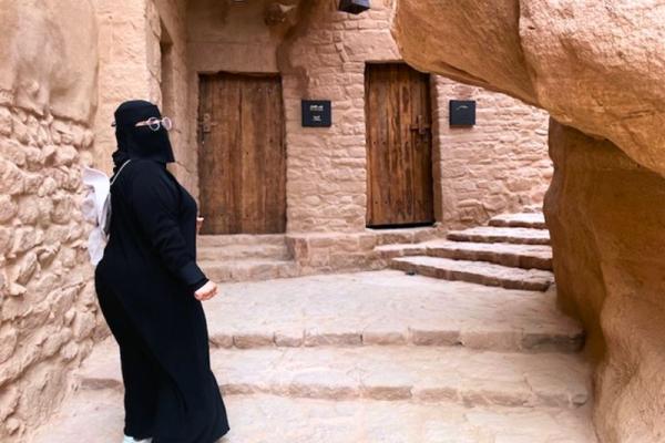 Hlinené mesto v oáze AlUla a miestna sprievodkyňa v čiernej abáji.
