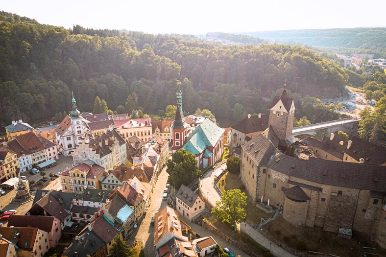 Hrad Loket a historické centrum mesta s farebnými domami a lesom v pozadí.