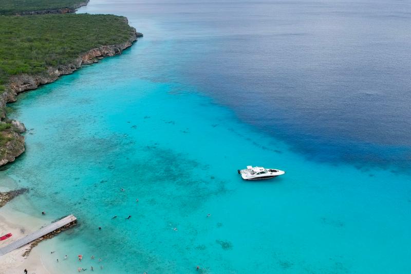 Nádherná tyrkysová farba mora, loď, zelené pobrežie a mólo na pláži. Curacao.