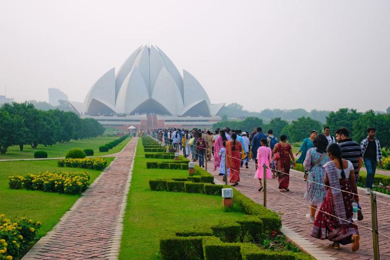 Lotus Temple v pozadí, park a kráčajúci ľudia v Indii.