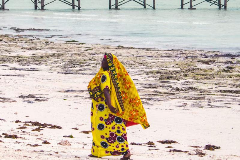 Černoška v žltých šatách na pláži na Zanzibare.