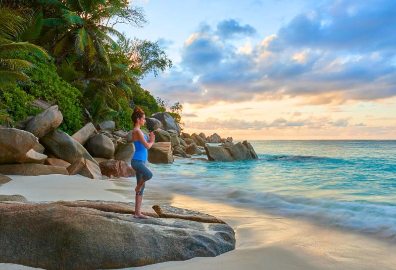 Piesková pláž a žena cvičí jogu na ostorve Seychely.
