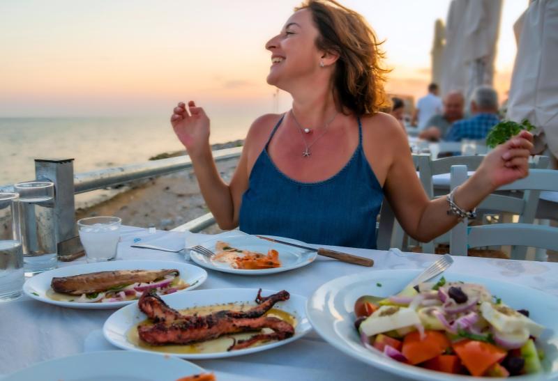 Žena za stolom v reštaurácii pri mori pri západe slnka.