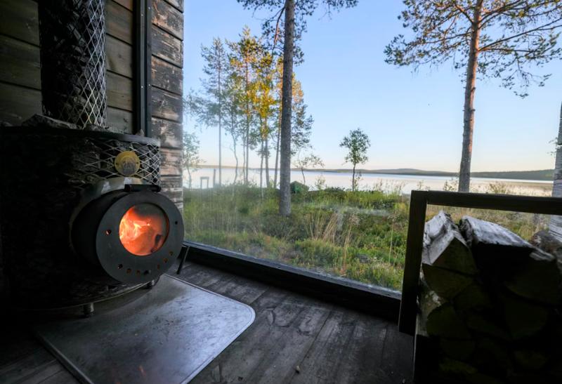 Vnútro fínskej sauny, pec, drevo a výhľad na východ slnka v prírode.