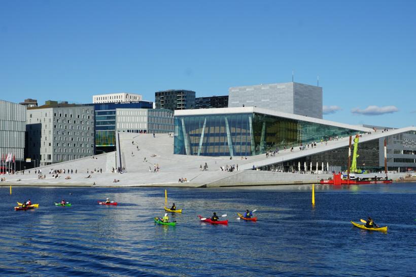 Ľudia na kajakoch na mori a moderné budovy v Oslo.