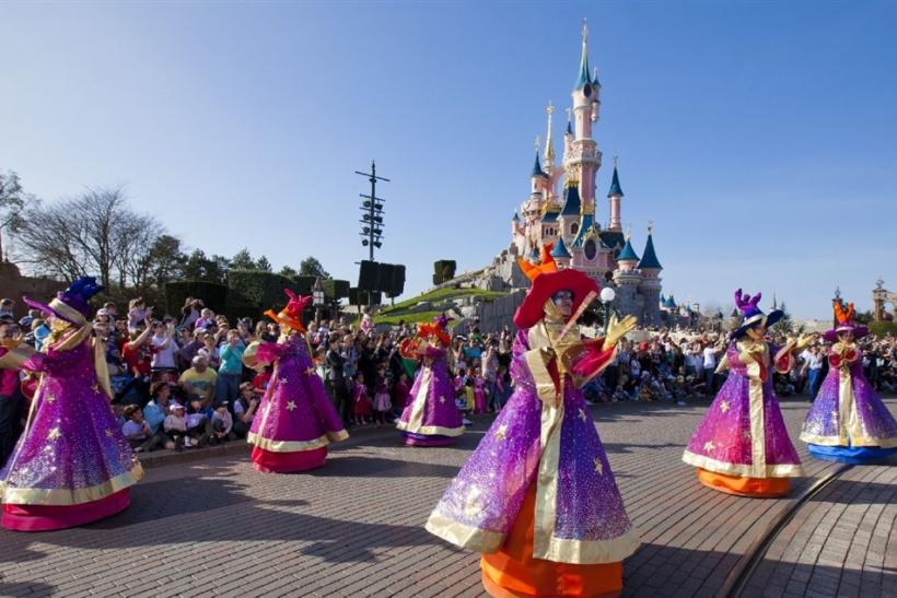 Ľudia v Disneylande s tanečnicami a zámkom v pozadí.