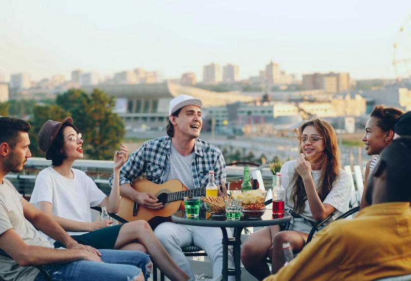 Ľudia sediaci v kruhu za stolom a muž s gitarou.