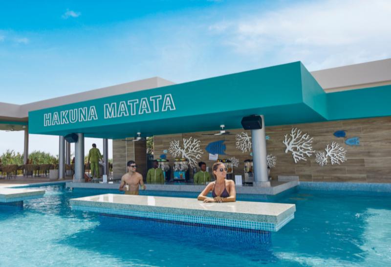Bazén a bar s nápisom Hakuna Matata a ľudia vo vode.