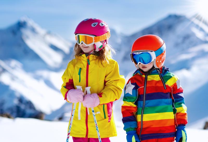 Dve malé deti vo farebných zimných odevoch na svahu.