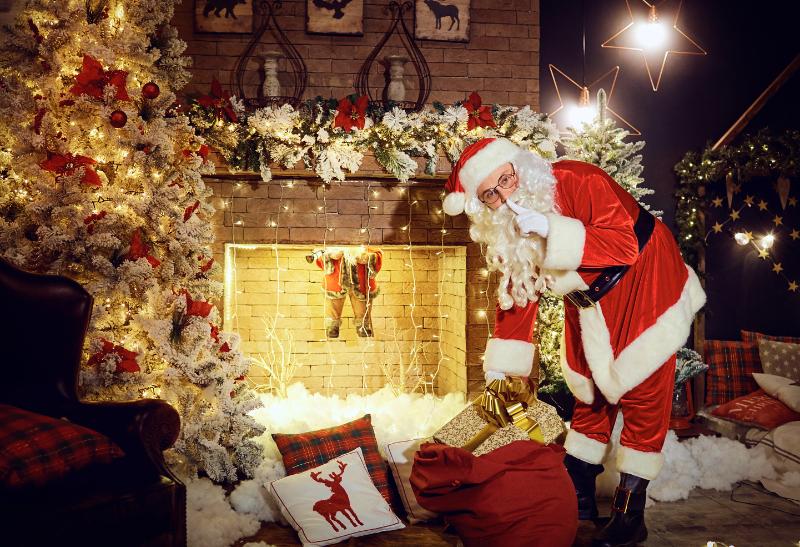 Santa Clasu s bielou bradou pri stromčeku a pri krbe.