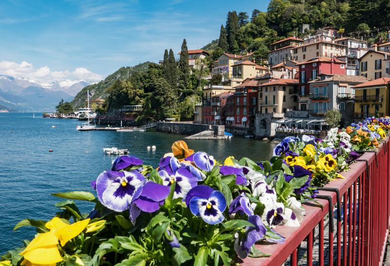 Farebné domy, kvety a jazero s horami v Taliansku.