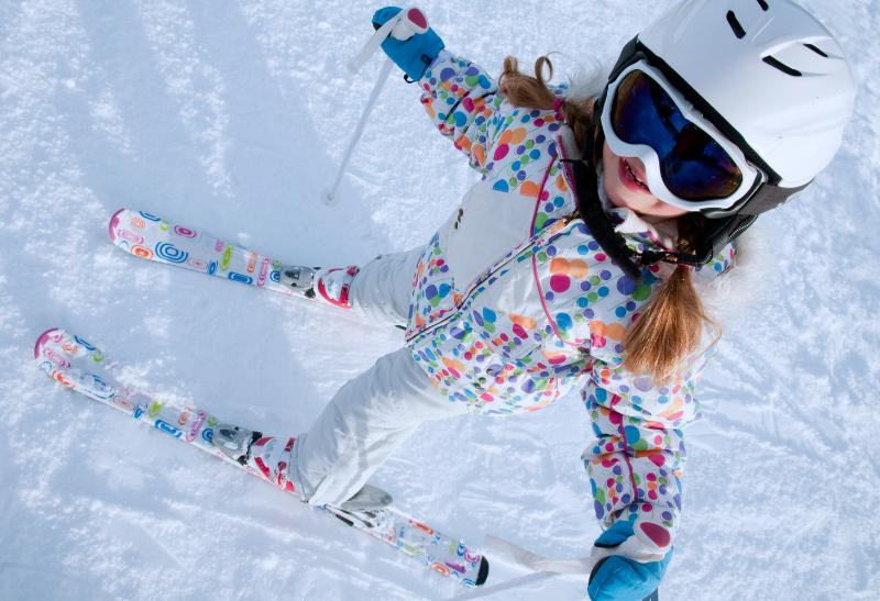 Malá lyžiarka s lyžami na snehu a lyžiarskej prilbe a okuliaroch.