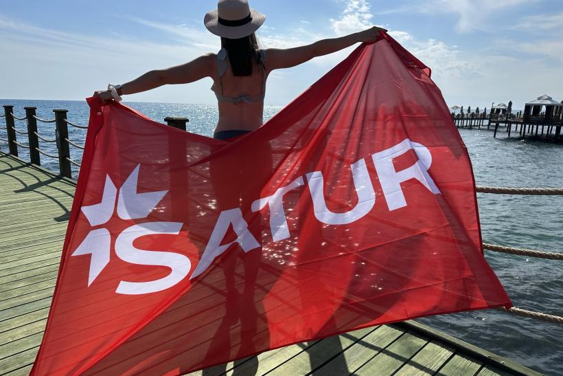 Žena na drevenom móle na pláži s nápisom SATUR v Turecku.