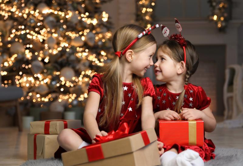 Dve malé dievčatká a vyzdobený a svietiaci vianočný stromček v dome.