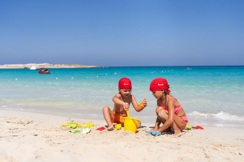 Dve malé deti na bielom piesku s hračkami a pri blankytnom mori v Marsa Matrouh v Egypte.