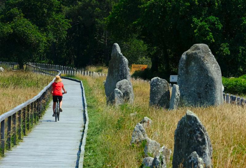 Žena na bicykli na drevenom chodníku v Carnacu.