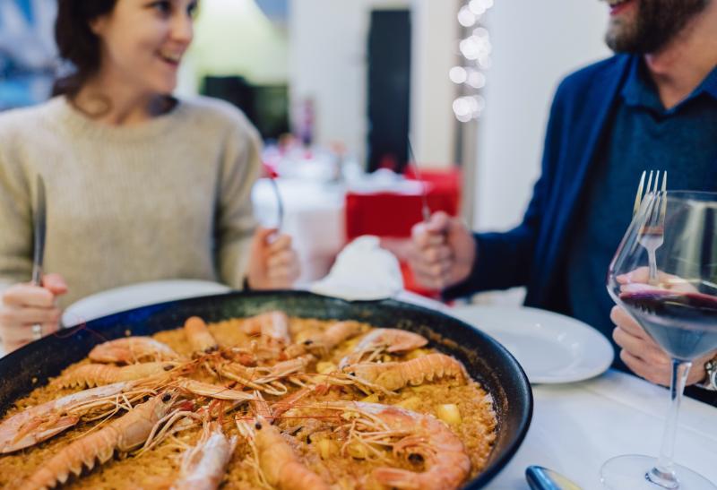 Pár za stolom s vínom a paellou.