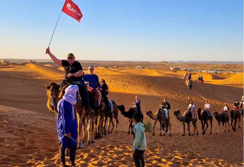 Skupina ľudí jazdí na ťavách na dunách v Maroku.