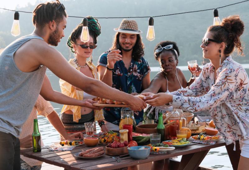 Muži a ženy okolo stola s jedlom pri vode.