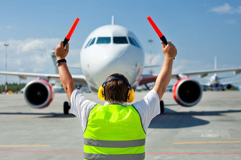 Pracovník letiska pred lietadlom ukazujúci zastavenie.