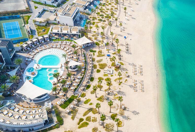 Hotel Nikki Beach Dubai s plážou, lehátkami, bazénom a tyrkysovým morom.