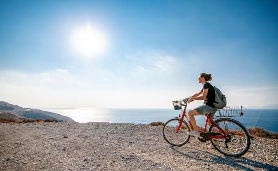 Mladá žena na bicykli pri pobreží s výhľadom na Egejské more na ostrove Kos, Grécko