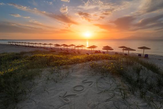 Romantický západ slnka nad piesočnou plážou s lehátkami a slnečníkmi na ostrove Kos, Grécko