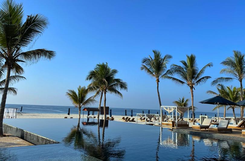 Kokosové palmy, piesková pláž, bazén a lehátka pred hotelom Al Baleed Resort Salalah by Anantara. Omán