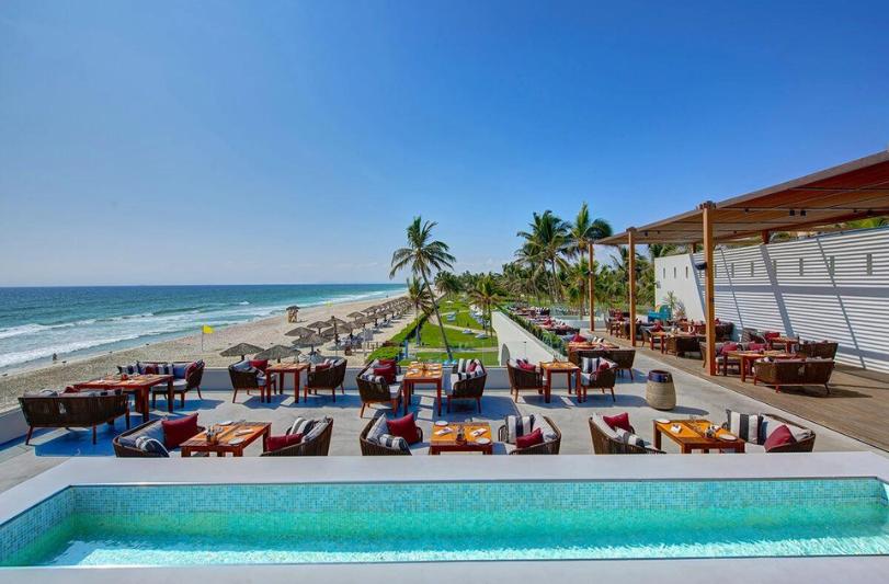 Piesočnatá pláž, palmy, otvorená reštaurácia hotela Crowne Plaza v Salalah. Omán