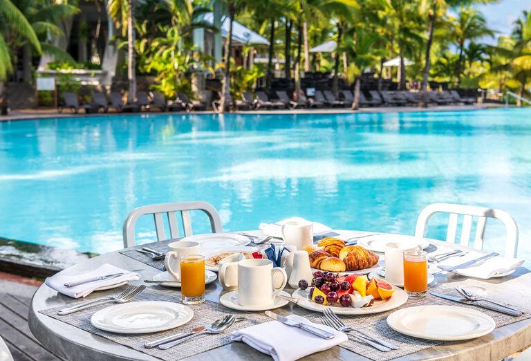 Raňajky na stole pri bazéne v očarujúcom prostredí hotel Victoria Beachcomber. Maurícius.