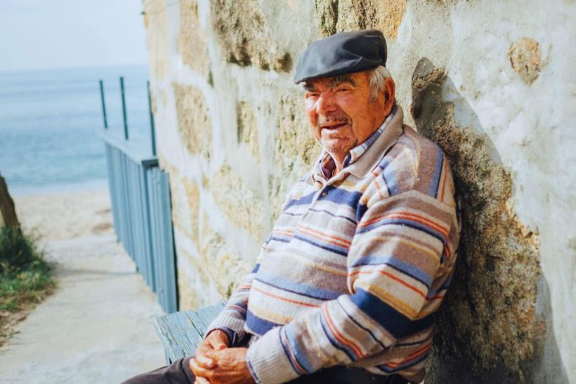 starý Grék v svetri sediaci na lavičke pri mori