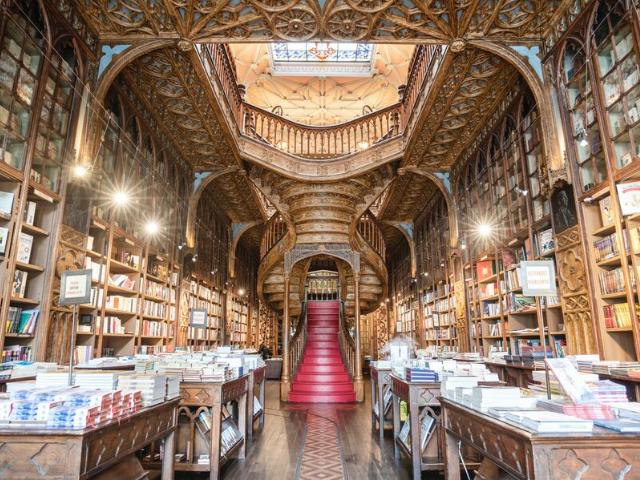 Rozprávkové kníhkupectvo v Porte s naukladanými knihami v regáloch, s vyrezávaným stropom a schodiskom.