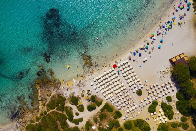 Piesková pláž, priezračné more a hotelové ležadlá a slnečníky. Sardínia