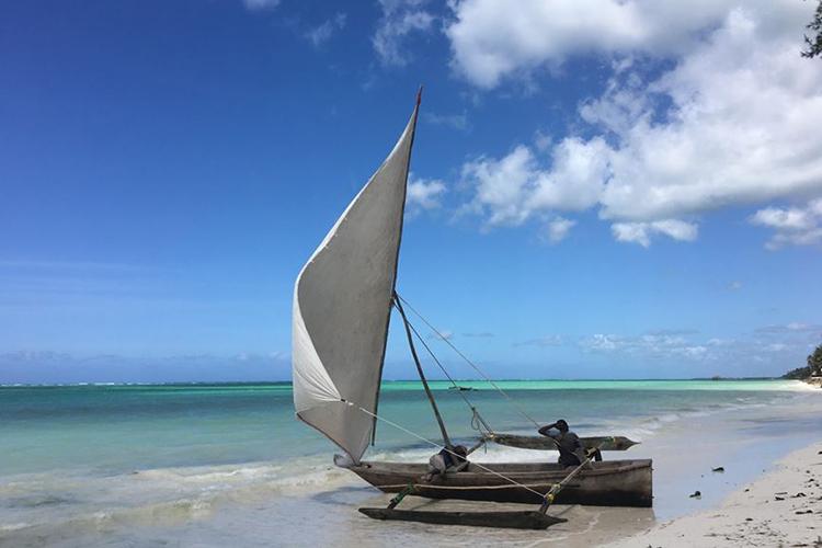 Piesková pláž a drevená loď na brehu na ostrove Zanzibar.