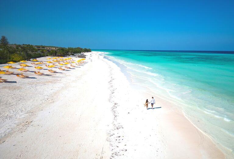 Exotický Zanzibar s bielymi plážami, lehátkami a prechádzajúci sa pár.