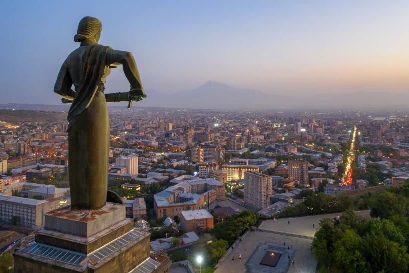 Socha, mesto Jerevan po západe slnka a pohorie Ararat v pozadí.