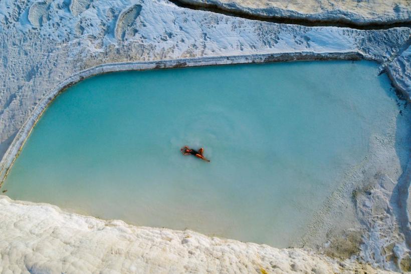 Tyrkysová voda v bielom prírodnom bazéne a žena vo vode v Pamukkale.