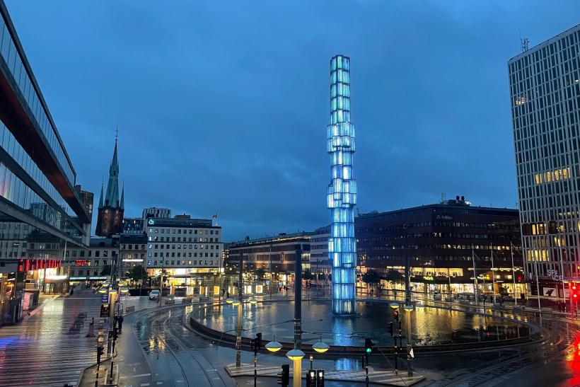 Námestie Sergels Torg vo večerných hodinách s moderným obeliskom.