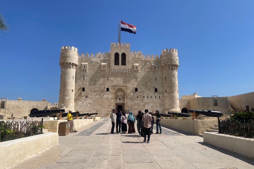 Pevnosť s vlajkou Egypta a turisti v Alexandrii.