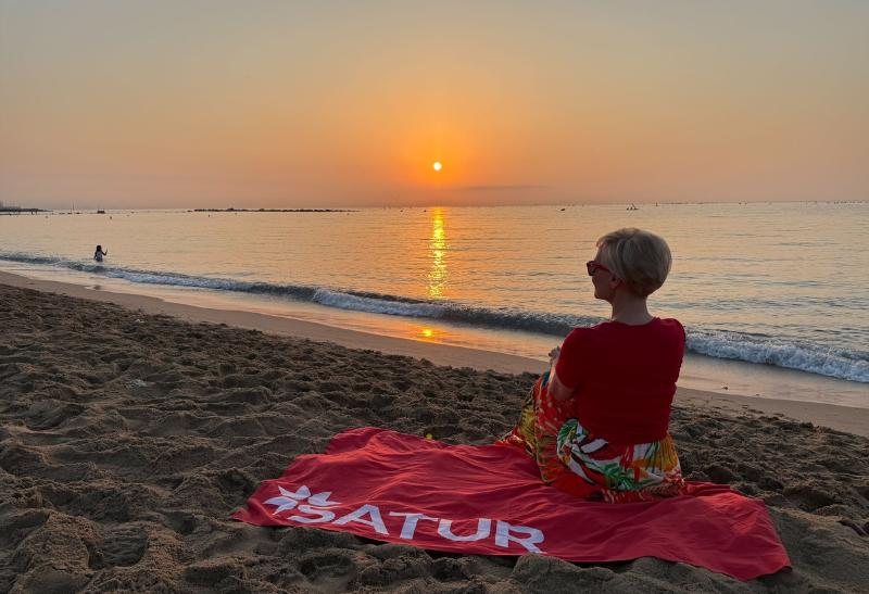 Žena sediaca na pláži v Barcelone pri západe slnka.